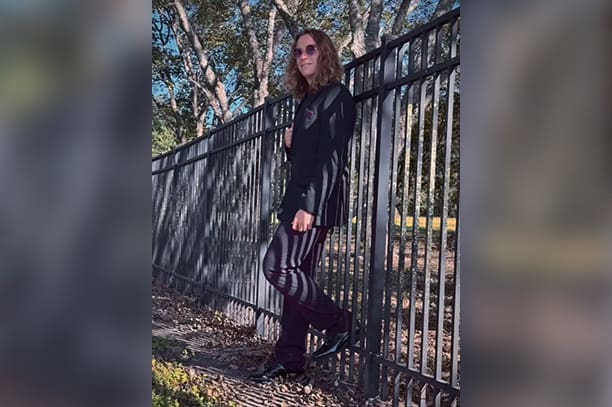 A woman standing next to a fence in the sun.