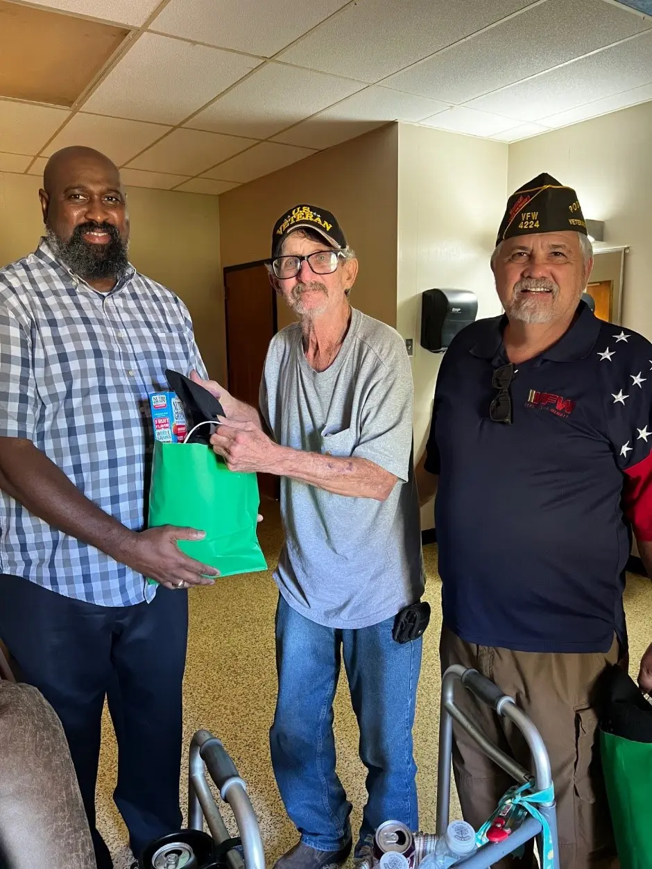 Three men standing in a room holding bags.